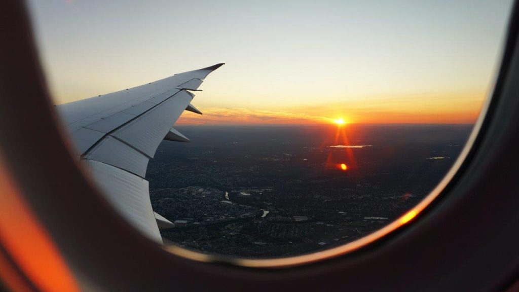 Aerial view of colorful sunset from airplane window, with clouds and horizon in sight.