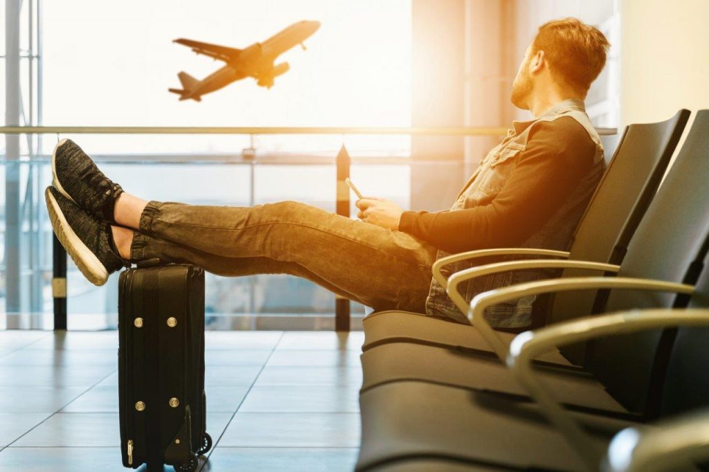 A man sitting on a chair with crossed legs, a suitcase in front of him.